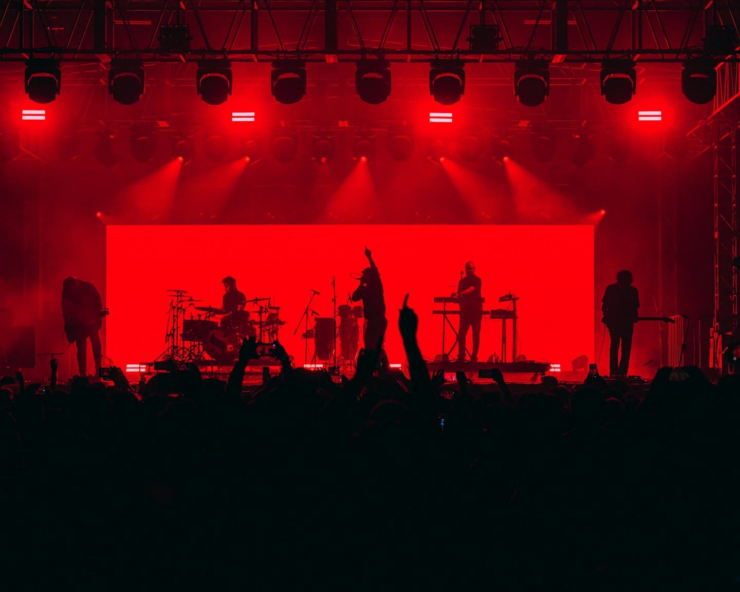 Musicisti suonano strumenti su un palco con uno sfondo rosso.