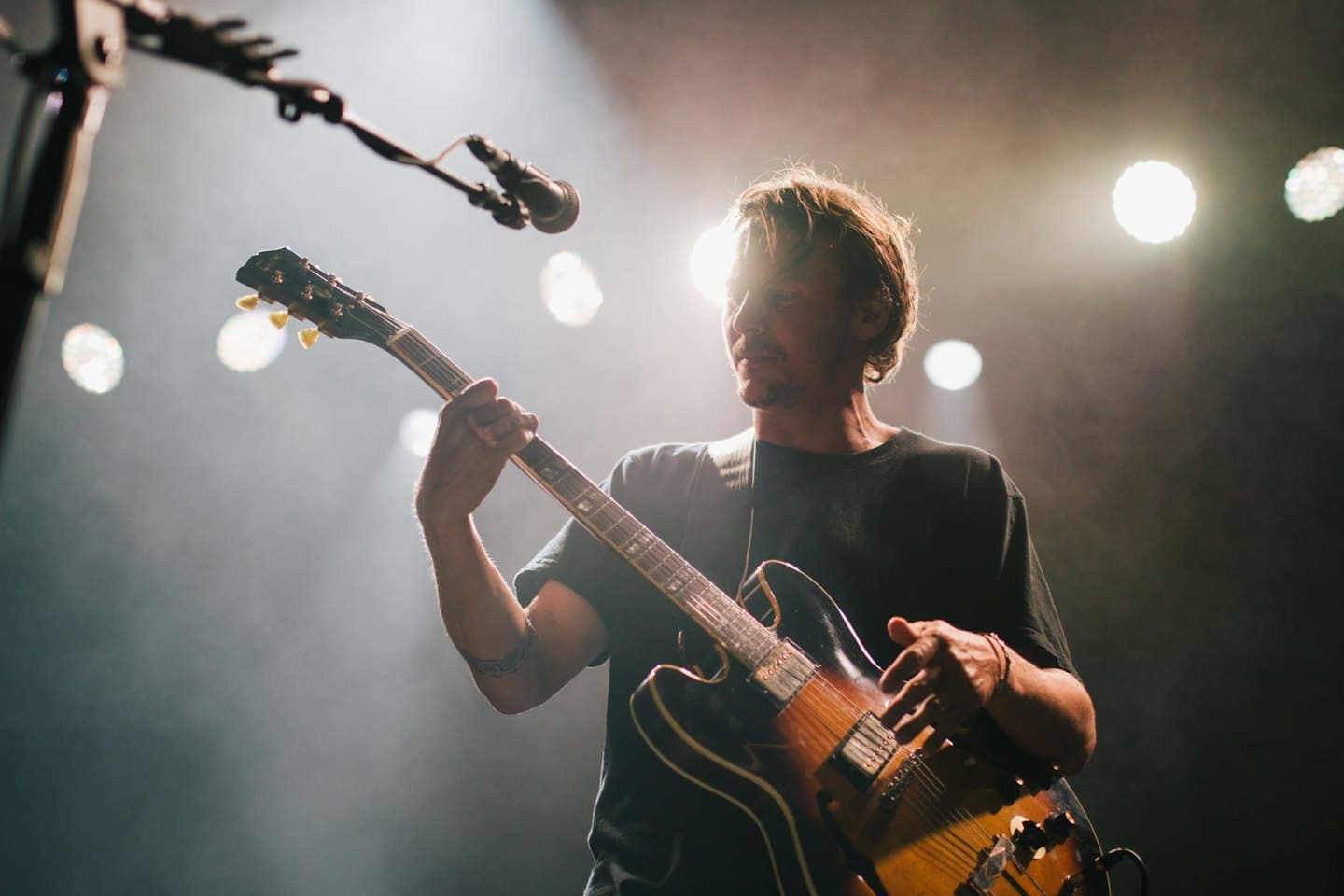 Uomo che suona la chitarra elettrica su un palco fumoso.